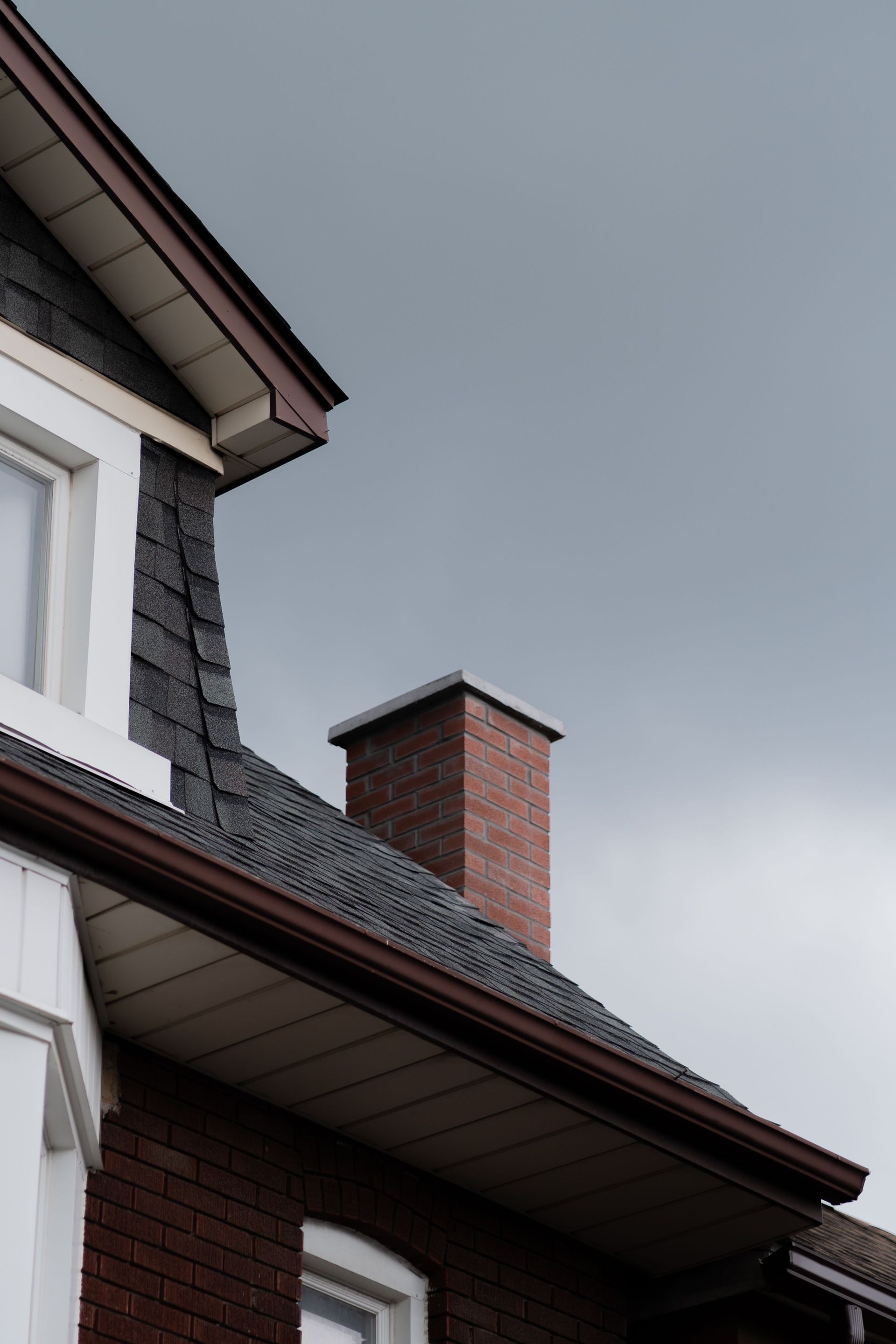 Brick chimney on a dark roof beside a white house under a cloudy gray sky