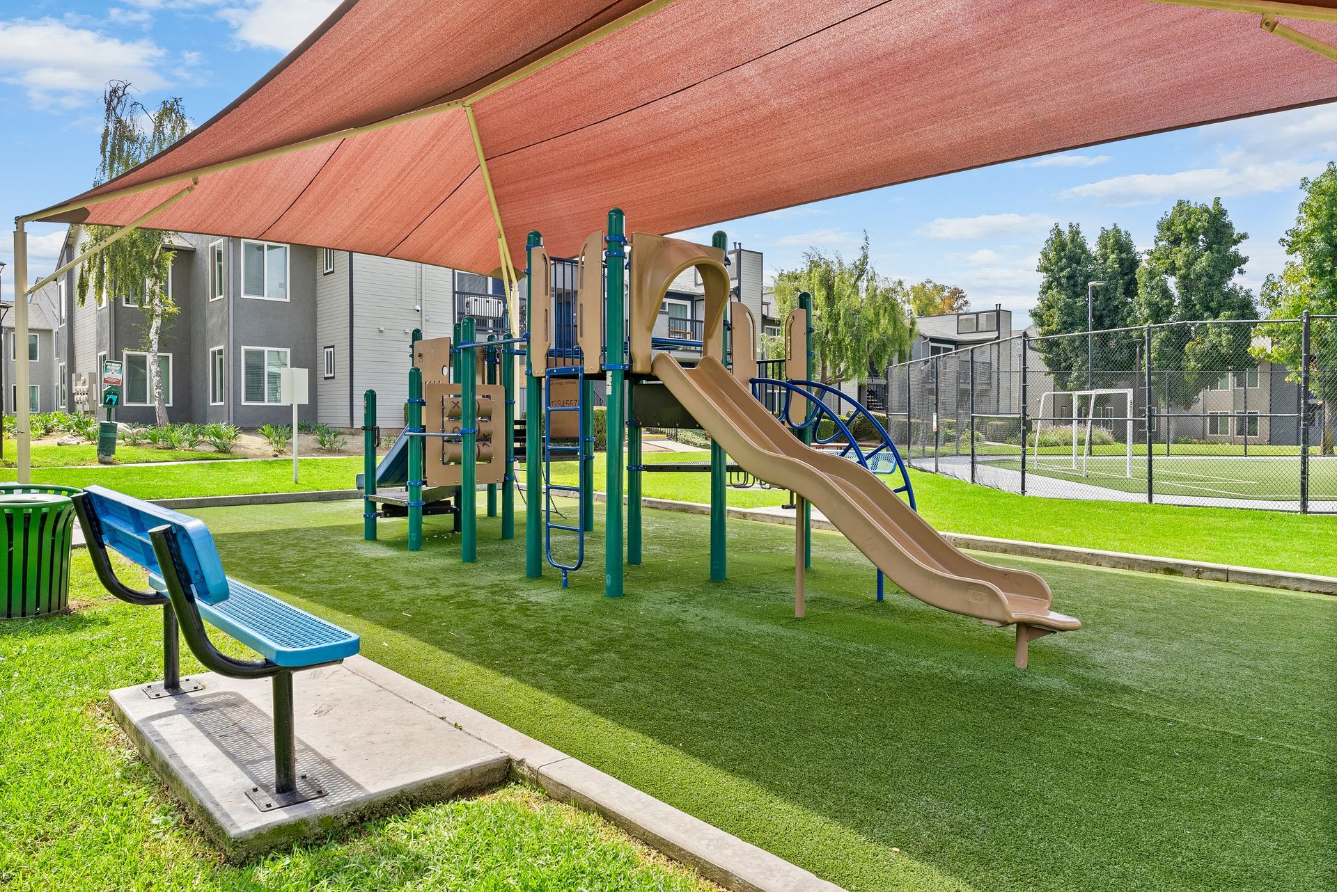 A playground with a slide and a bench under an umbrella.