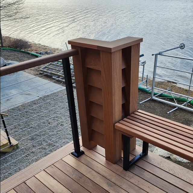Wooden deck with bench and built-in privacy wall near a lake, black metal railings, and a clear sky.