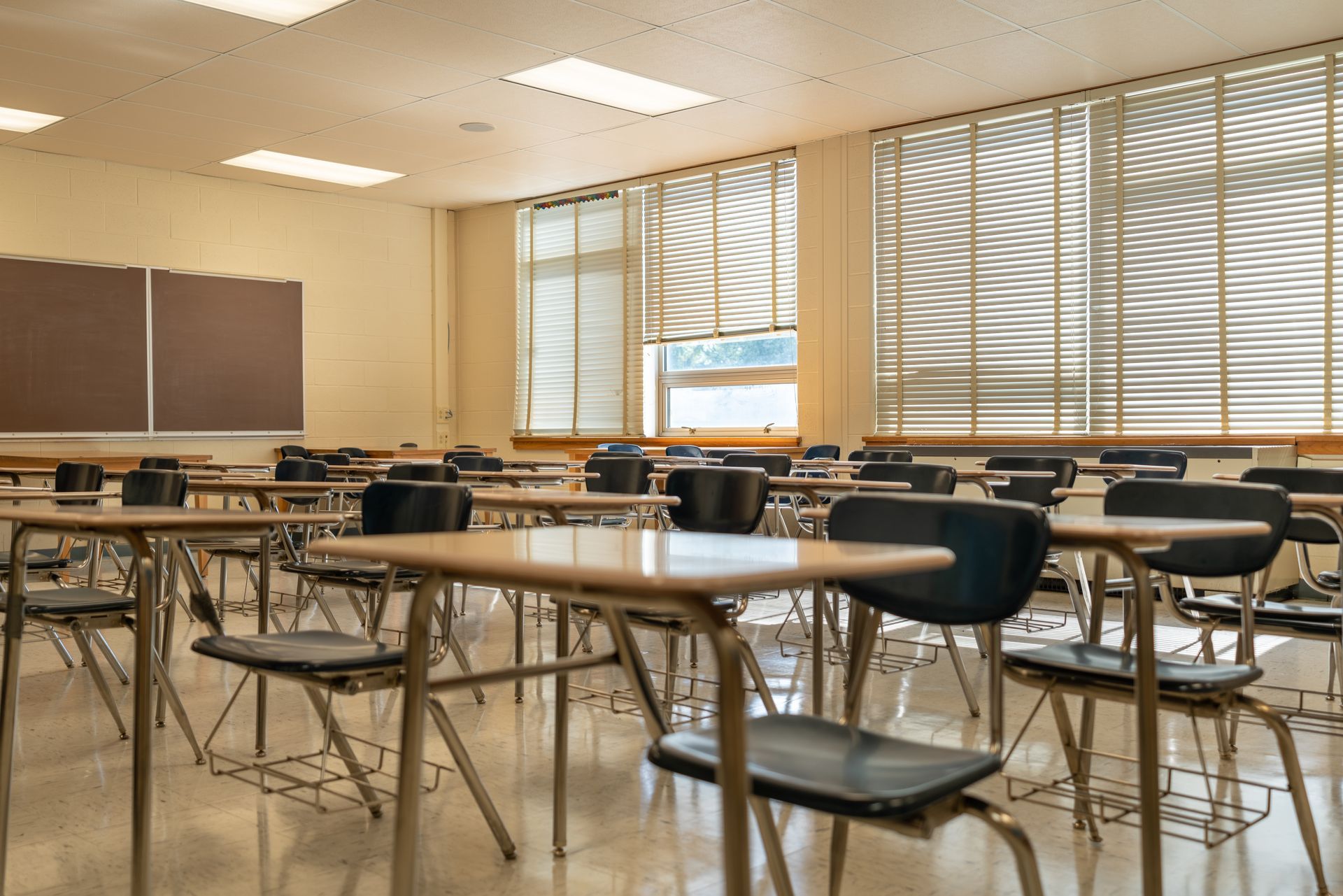 Une salle de classe vide avec des tables et des chaises et des stores aux fenêtres.