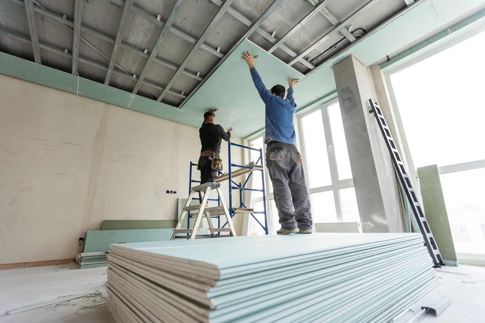 Deux hommes travaillent sur un plafond dans une pièce.