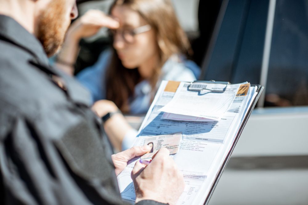 A man is writing on a clipboard in front of a woman in a car.