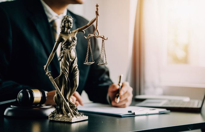 A man in a suit is sitting at a desk with a statue of justice.