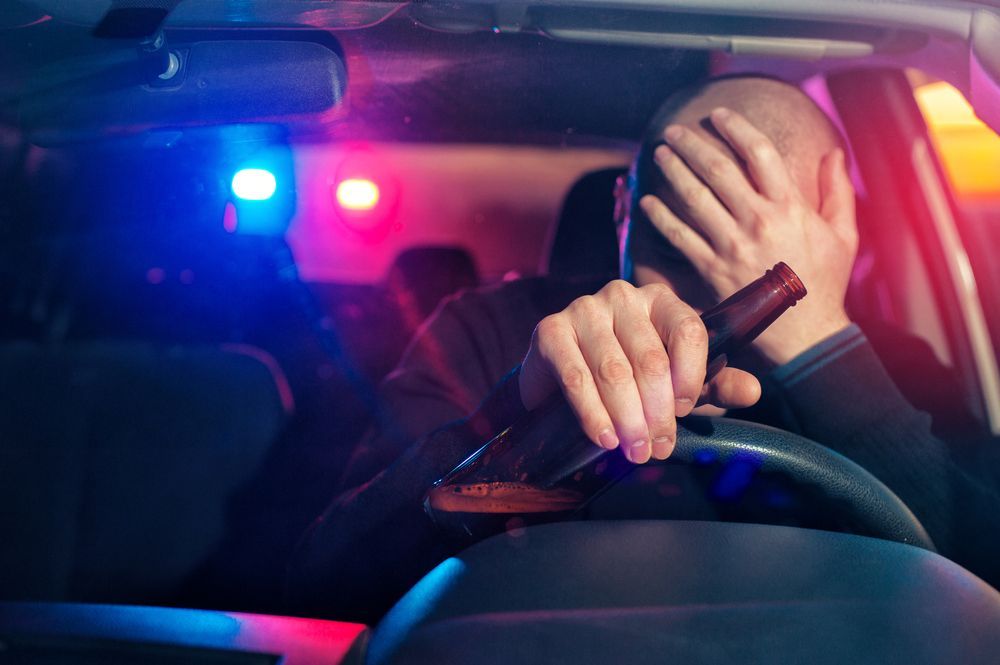 A man is holding a bottle of beer while driving a car.