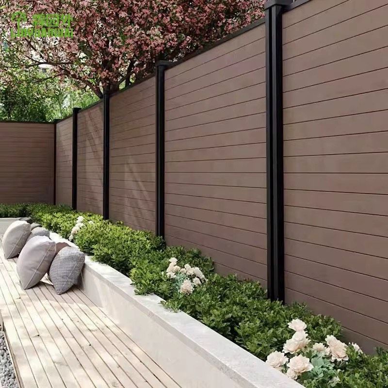 Wooden privacy fence with black posts, garden bed, and light-colored patio.