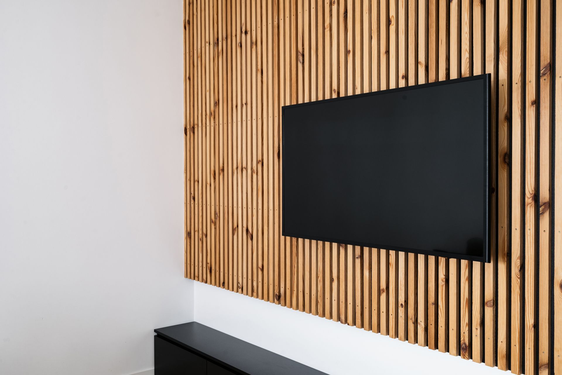 TV on wood slat wall, black cabinet below, white wall on left.