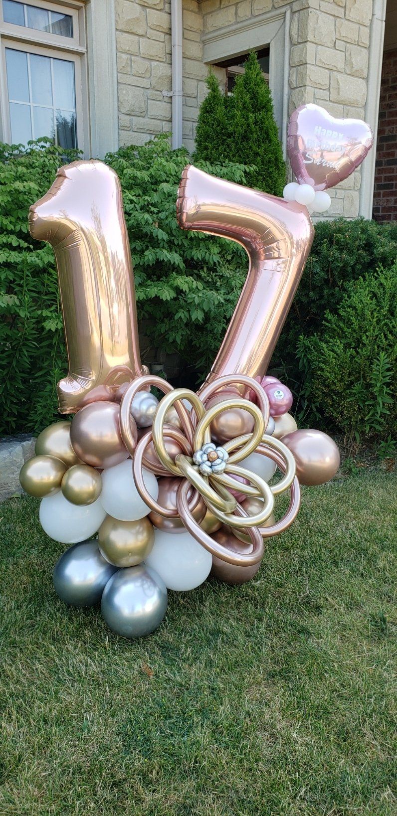 A bunch of balloons are sitting in the grass in front of a house.