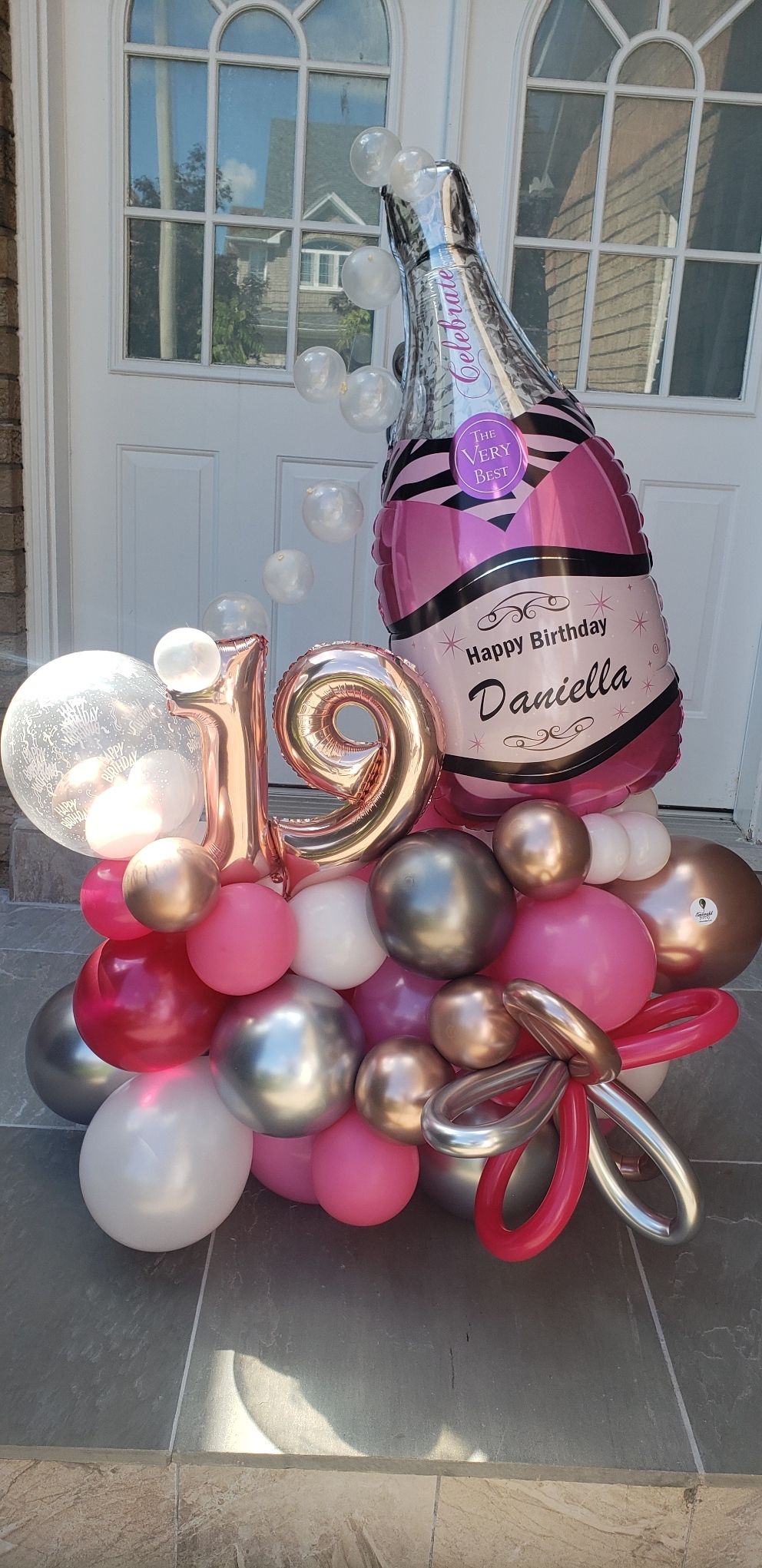 A bunch of balloons with a bottle of champagne on top of them.
