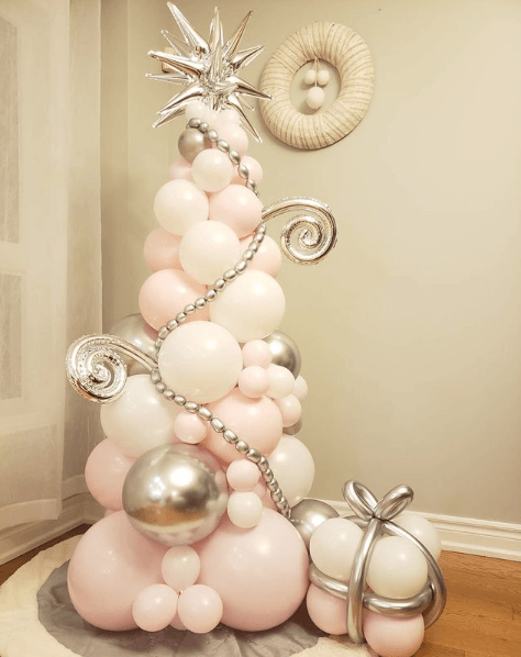 A pink and white balloon christmas tree is sitting on a rug in a room.