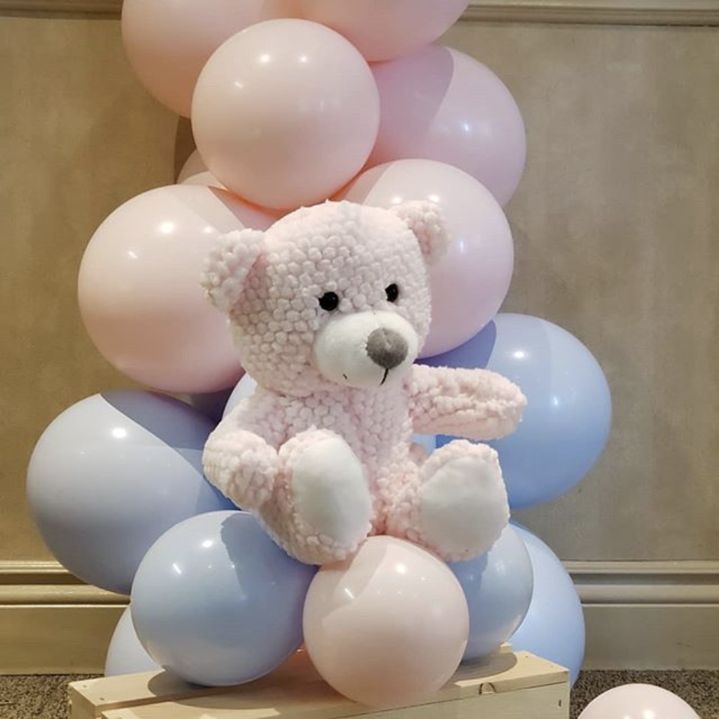 A teddy bear is sitting on top of a bunch of pink and blue balloons