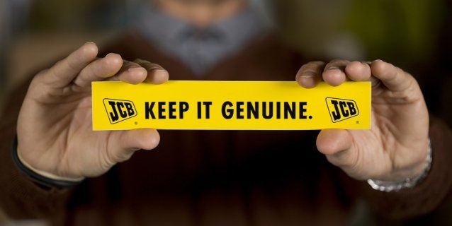 A pair of hands holding a bright yellow label up to the camera. The label says 'Keep it genuine'.