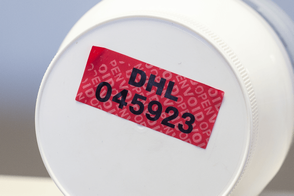 A white container with a red tamper evident label stuck to the bottom of it