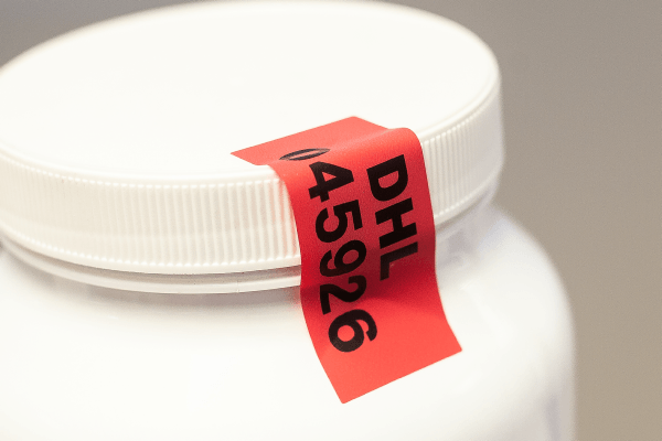 A white container with a red tamper evident label securing the lid