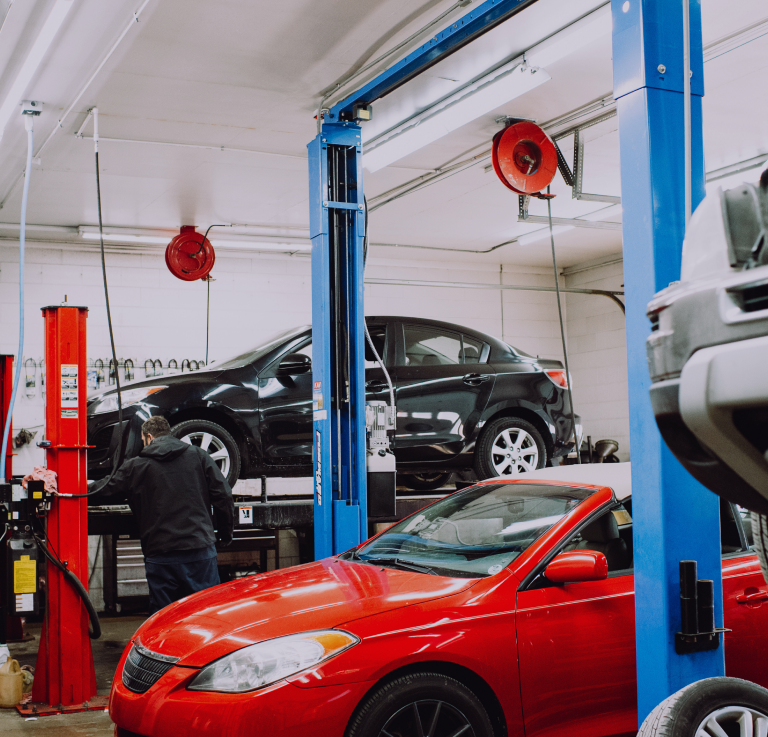 Auto repair shop with black and red cars on lifts and a mechanic working nearby | Mears Automotive