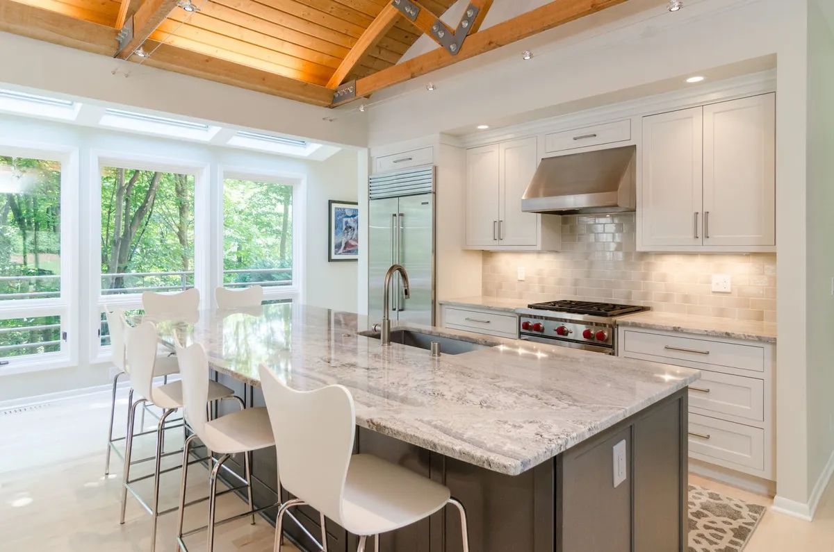 A kitchen with white cabinets , granite counter tops , stainless steel appliances and a large island.
