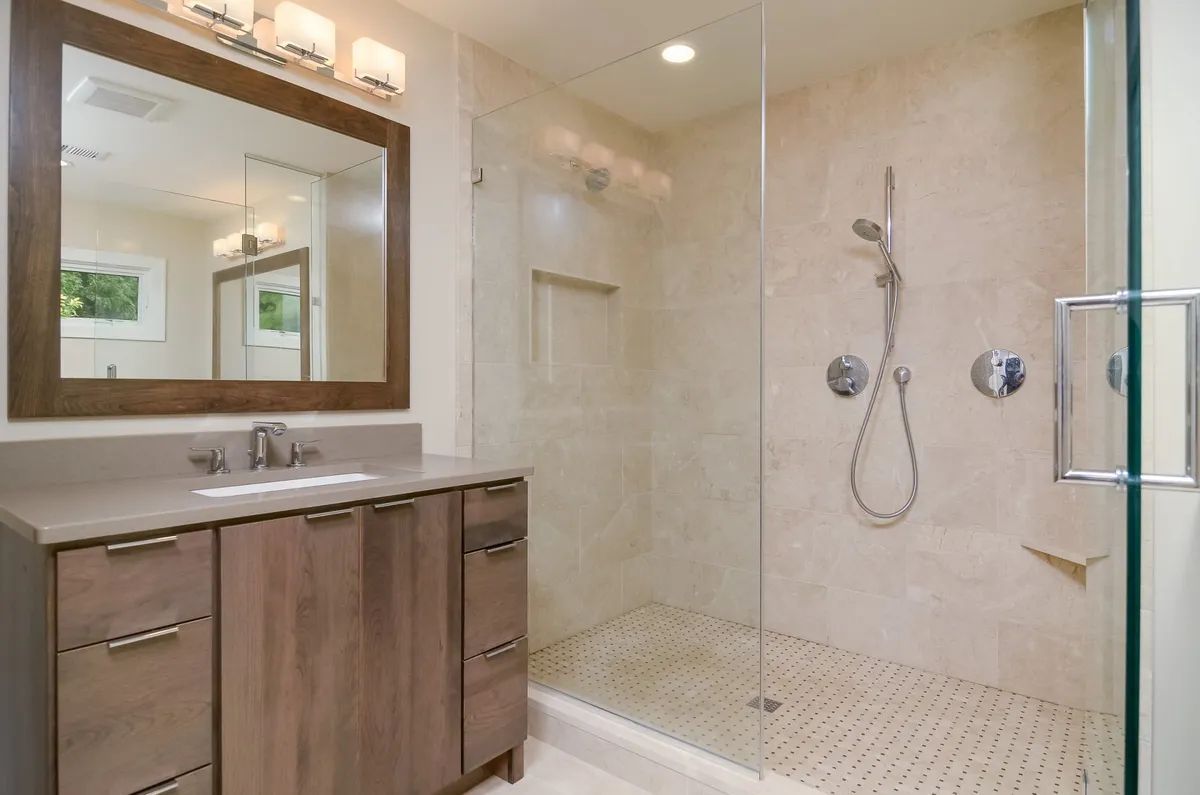 A bathroom with a sink , mirror and walk in shower.