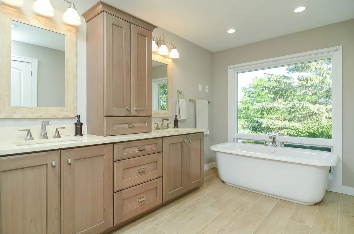 A bathroom with two sinks , a tub , a mirror and a window.