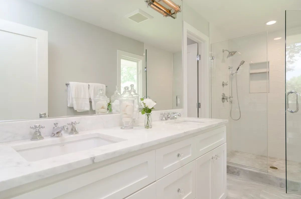 A bathroom with two sinks , a shower and a large mirror.