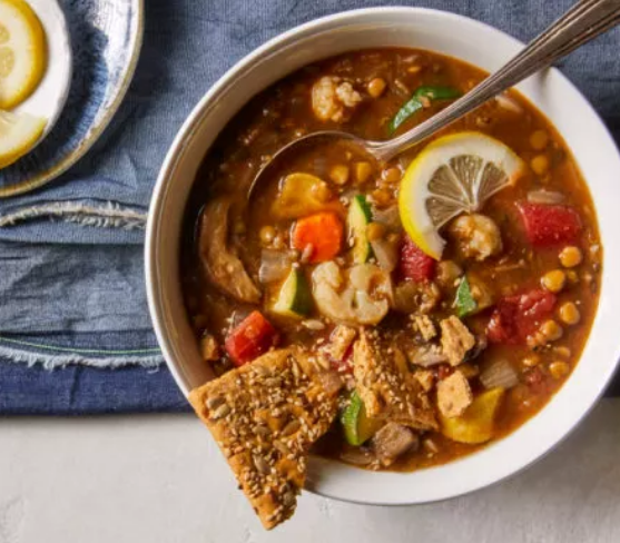 A bowl of soup with a spoon and a cracker in it.