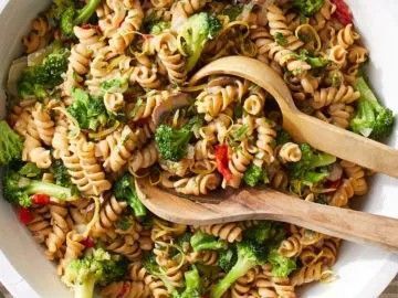 A bowl of pasta with broccoli and mushrooms and two wooden spoons.