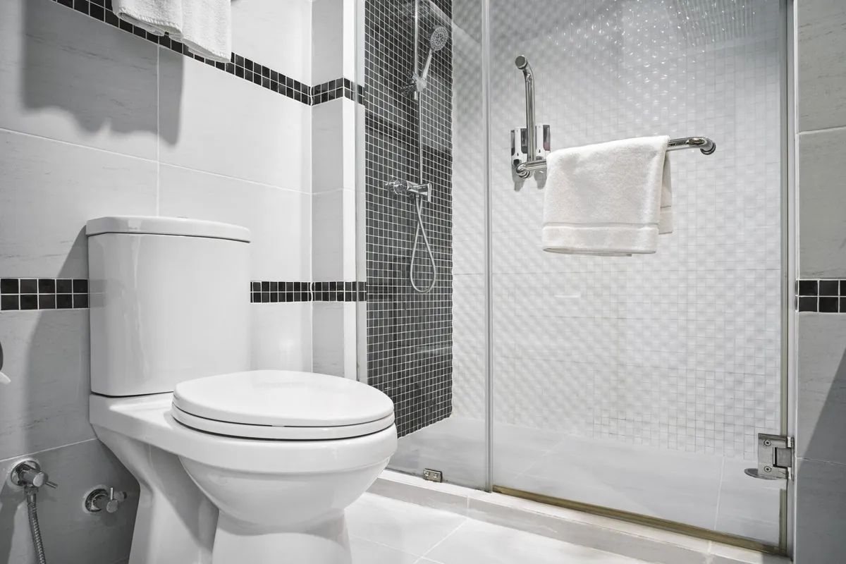 A bathroom with a toilet , shower , and towel rack.