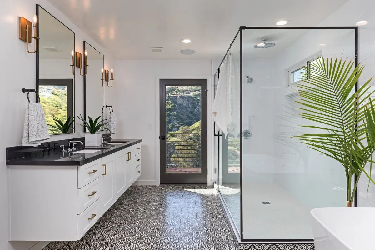 A bathroom with a walk in shower , two sinks , two mirrors and a tub.