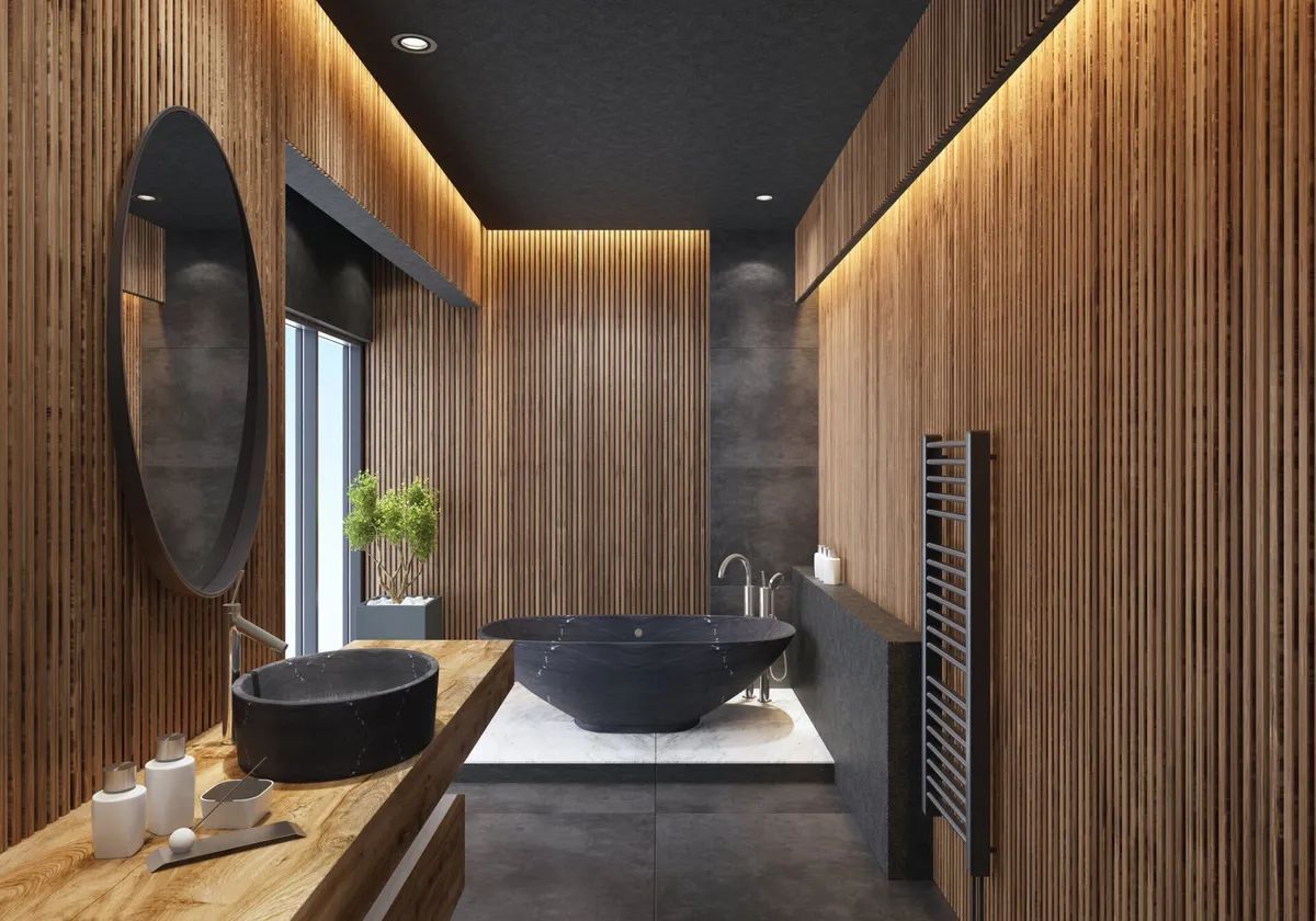 A bathroom with wooden walls , a black tub , a sink and a mirror.