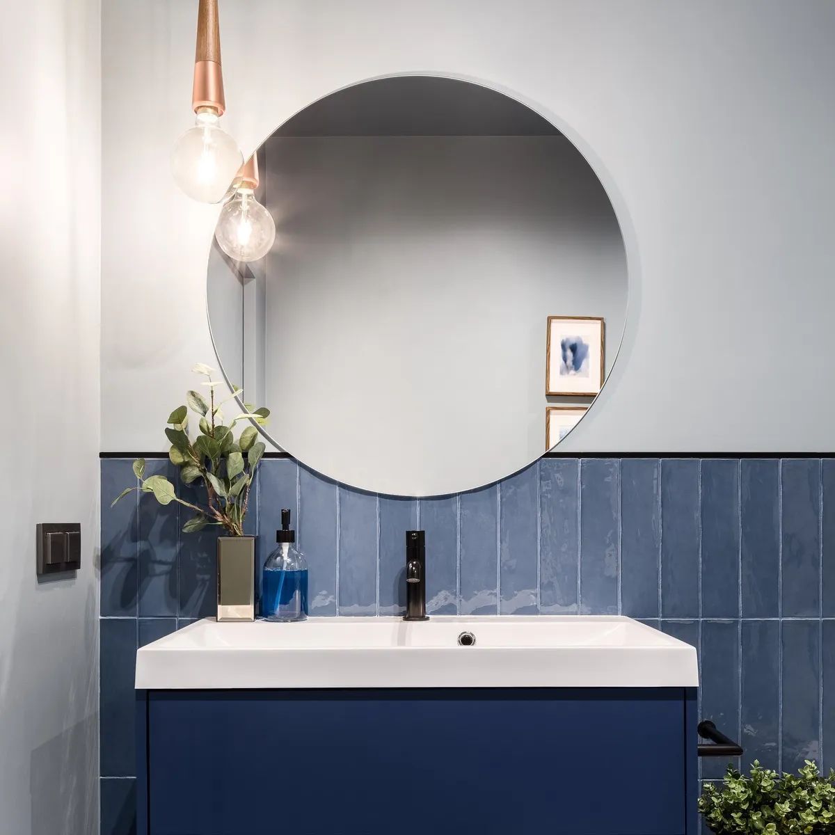 A bathroom with blue tiles and a round mirror