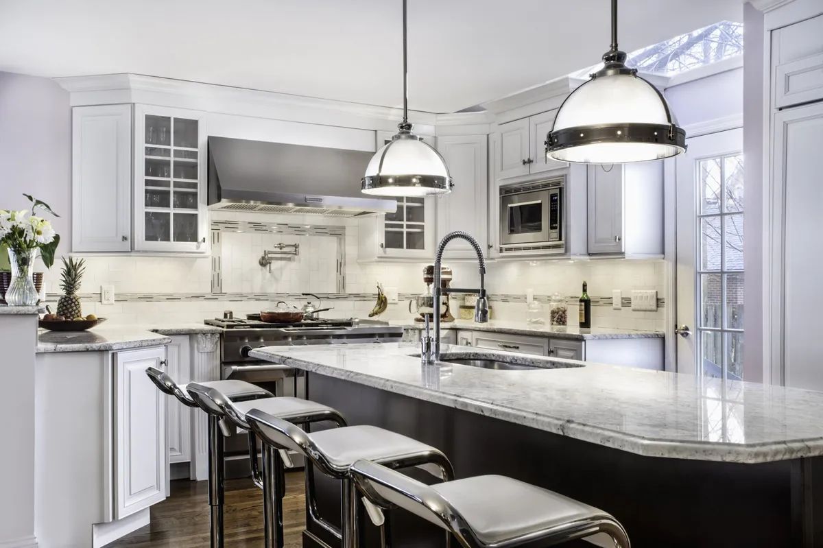A kitchen with white cabinets , stainless steel appliances , a large island and stools.
