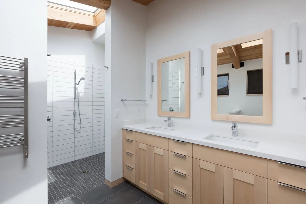 A bathroom with two sinks , two mirrors and a walk in shower.