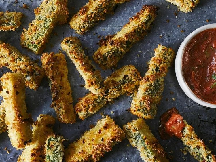 A bunch of zucchini sticks are sitting on a table next to a bowl of dipping sauce.