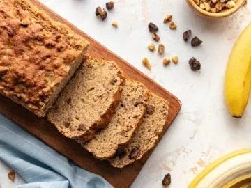 A loaf of banana bread is sitting on a wooden cutting board.