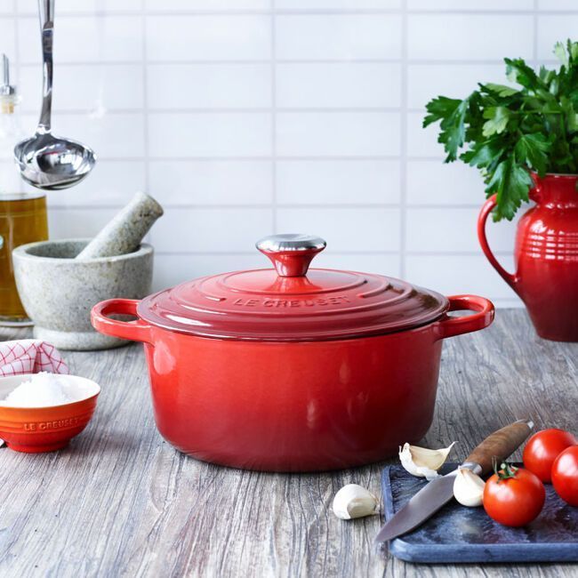 A red le creuset pot sits on a wooden table