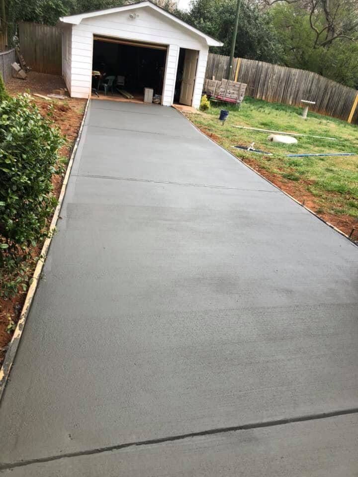 A concrete driveway leading to a garage in a backyard.