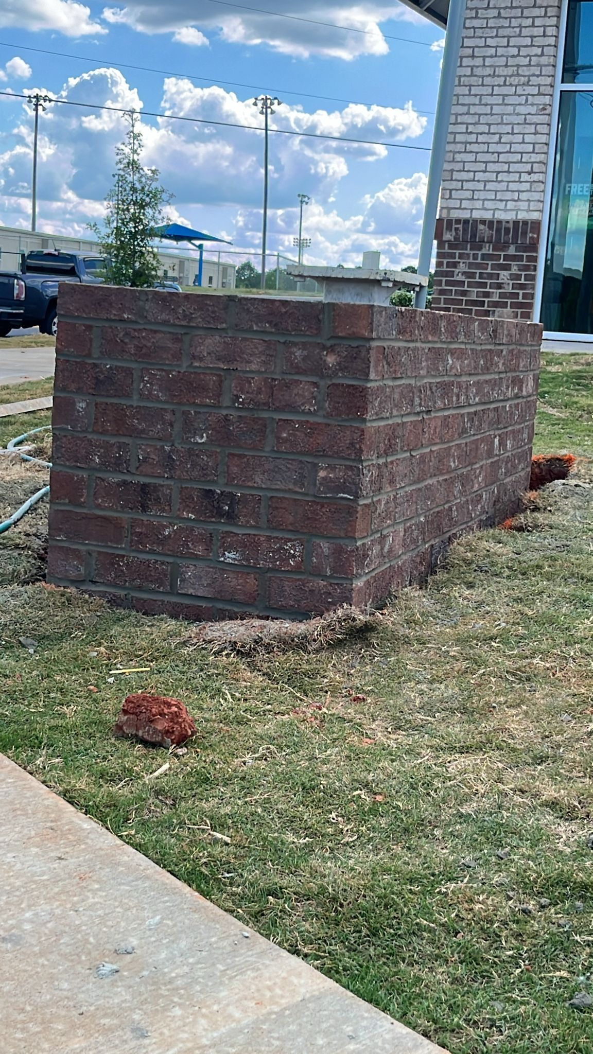 A brick wall is sitting in the grass next to a sidewalk.