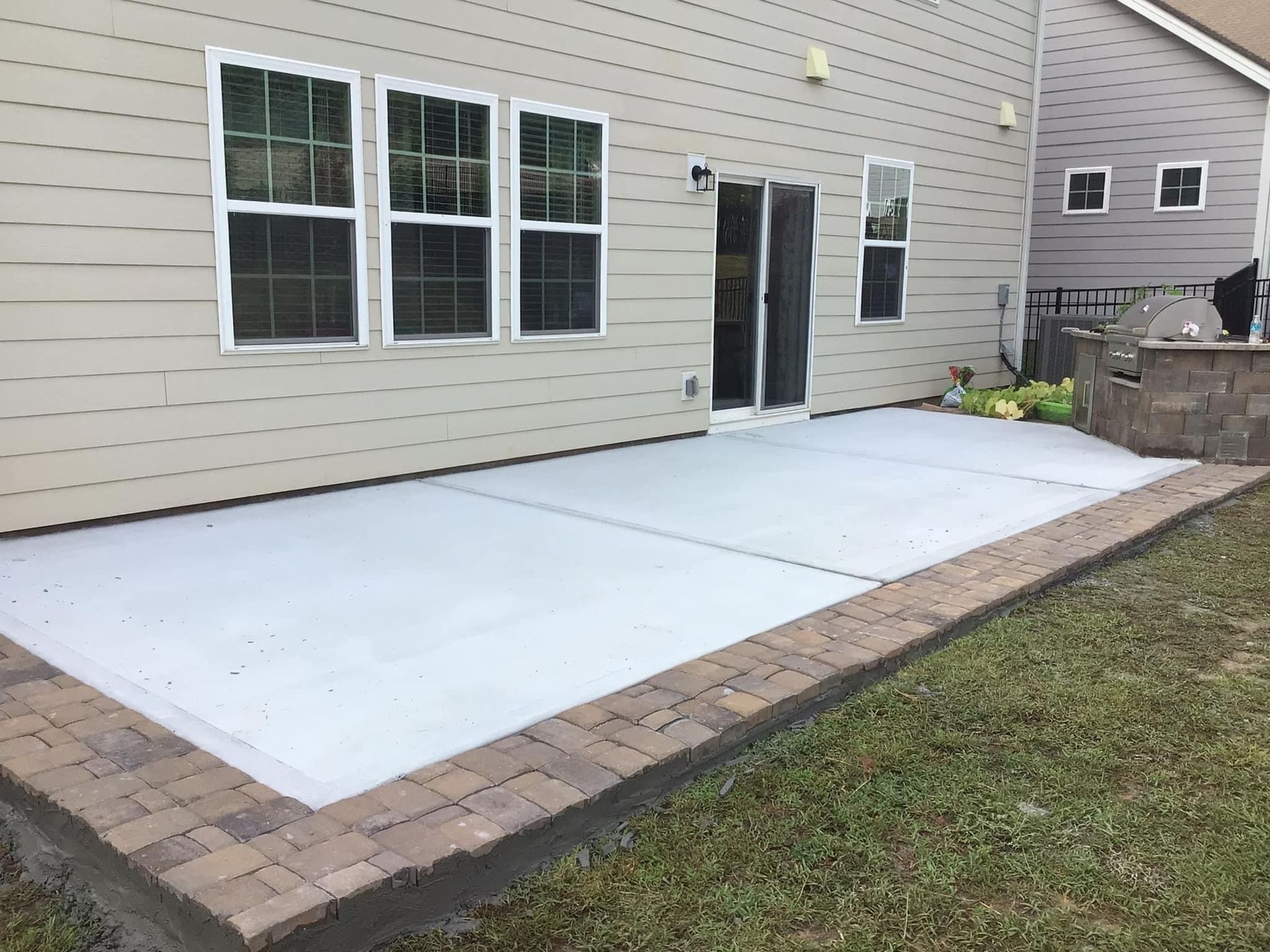 A patio with a brick border is in front of a house.