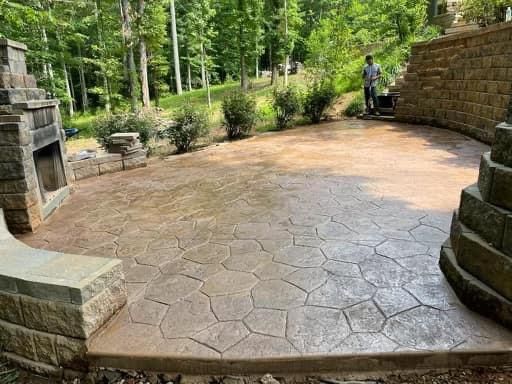 A man is standing on a concrete patio next to a fireplace.