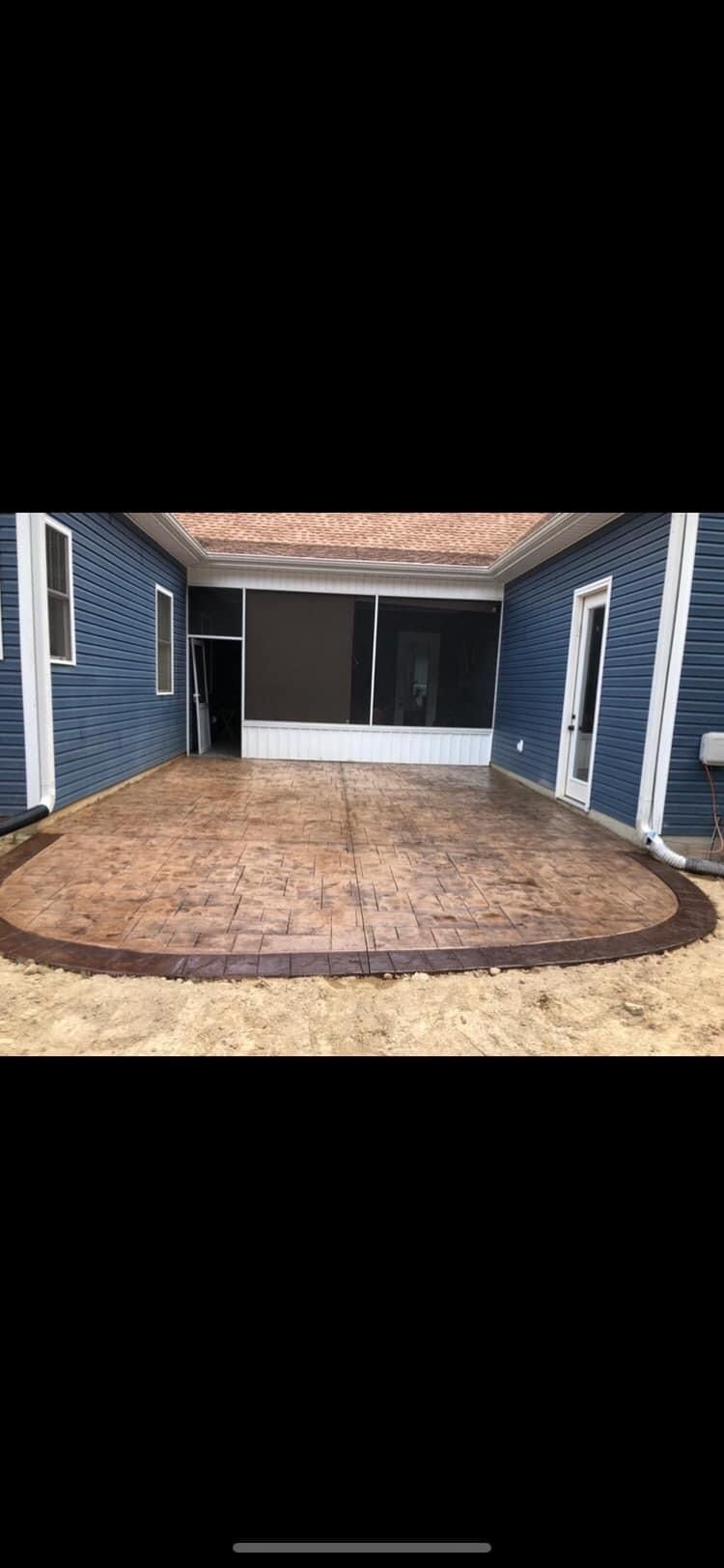 A concrete patio in front of a blue house with a screened in porch.