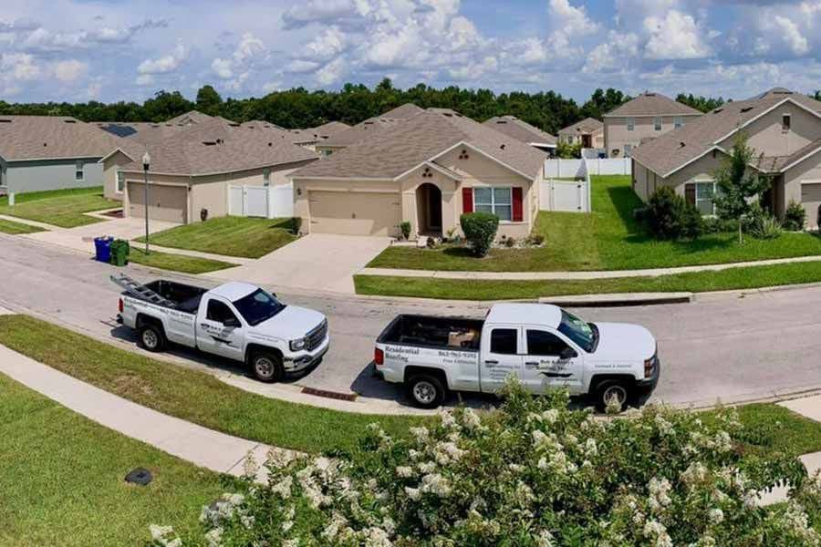 Two white trucks are parked on the side of the road in front of a residential neighborhood.