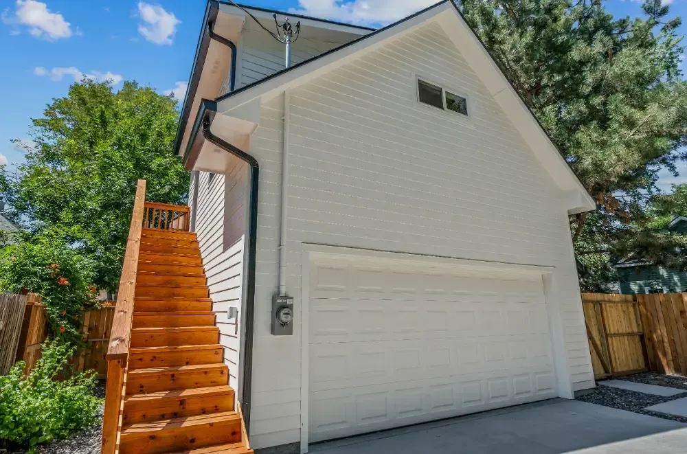 White two-story garage with wooden stairs, black gutters, and a blue sky.