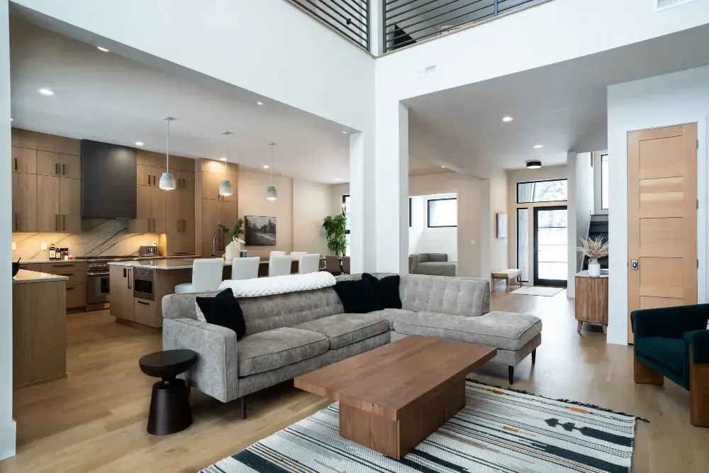 Spacious modern living room with kitchen. Light wood floors, grey sectional sofa, and a wooden coffee table.