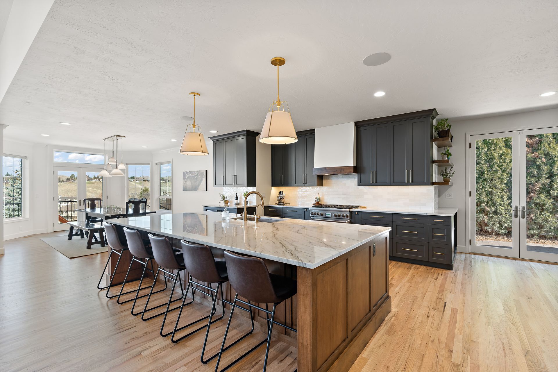 Modern kitchen with large island and seating, dark cabinets, light wood floor, and large windows.