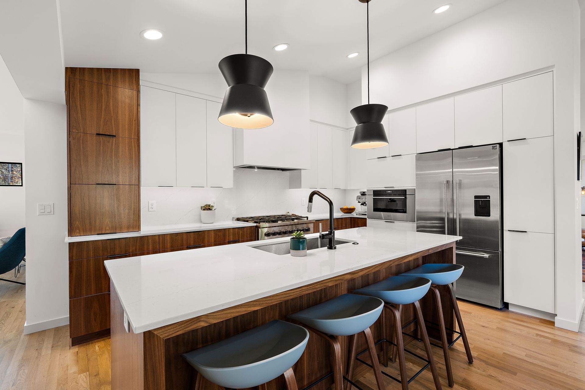 Modern kitchen with white and wood cabinetry, island with blue stools, stainless steel appliances.