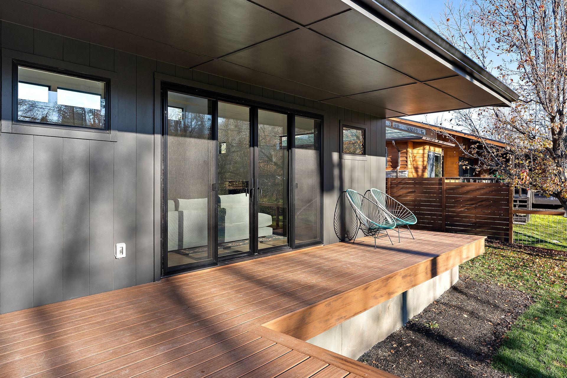 Modern home with a wood deck, sliding glass doors, and a small chair.