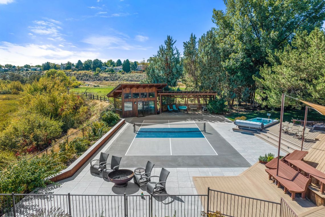 Outdoor patio with a pool, hot tub, and fire pit. Trees and a wooden structure in the background.