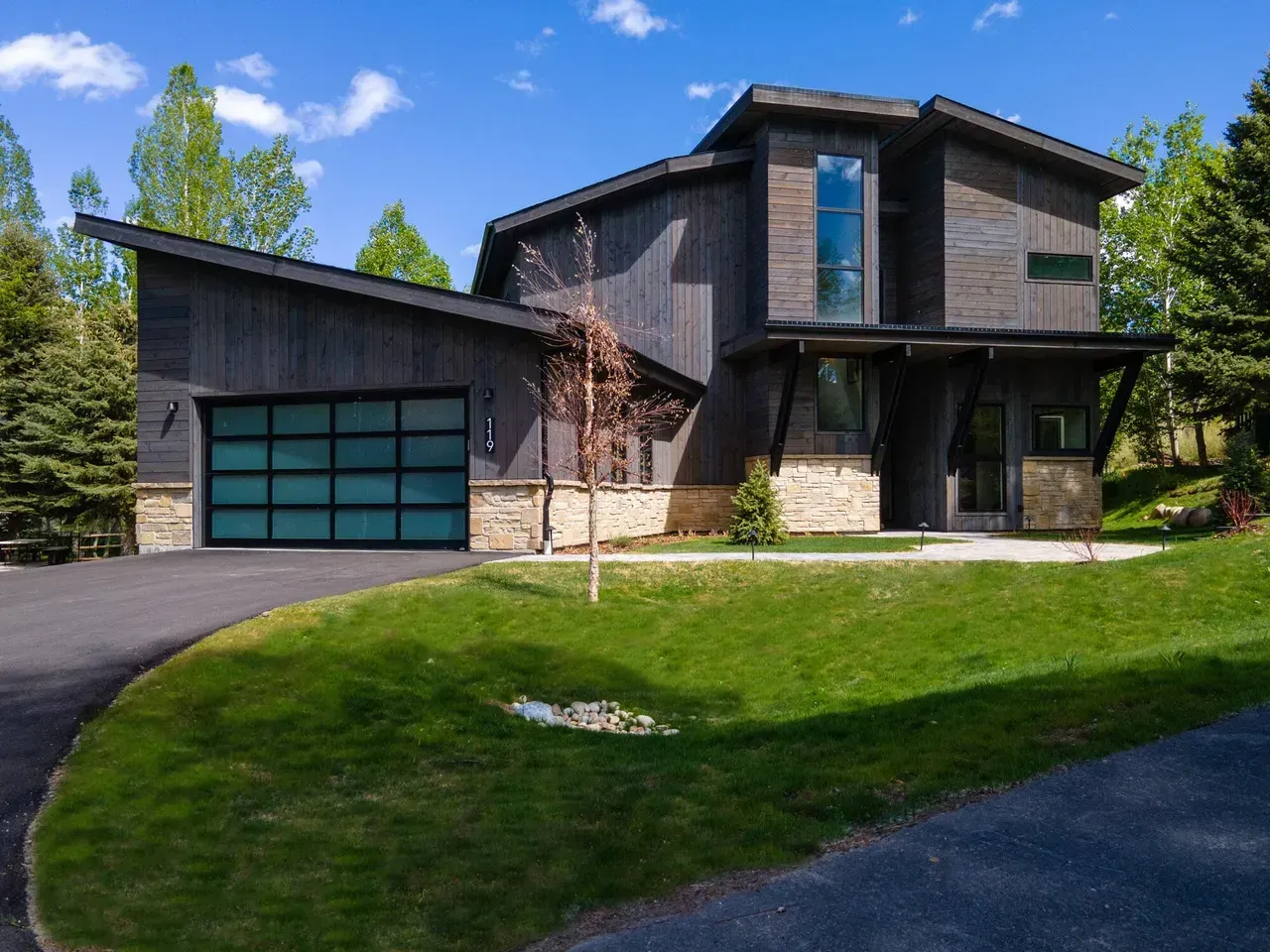 Mid-century modern house with white siding and dark roof, set on a slightly sloped lawn with trees.