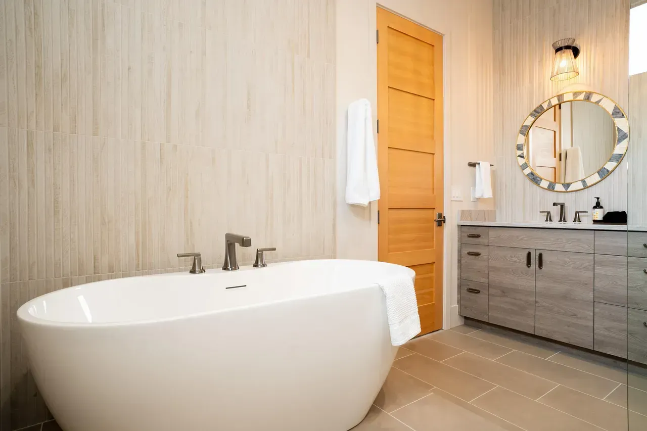 Bathroom with floral wallpaper, dual sinks, gold fixtures, and white cabinets.