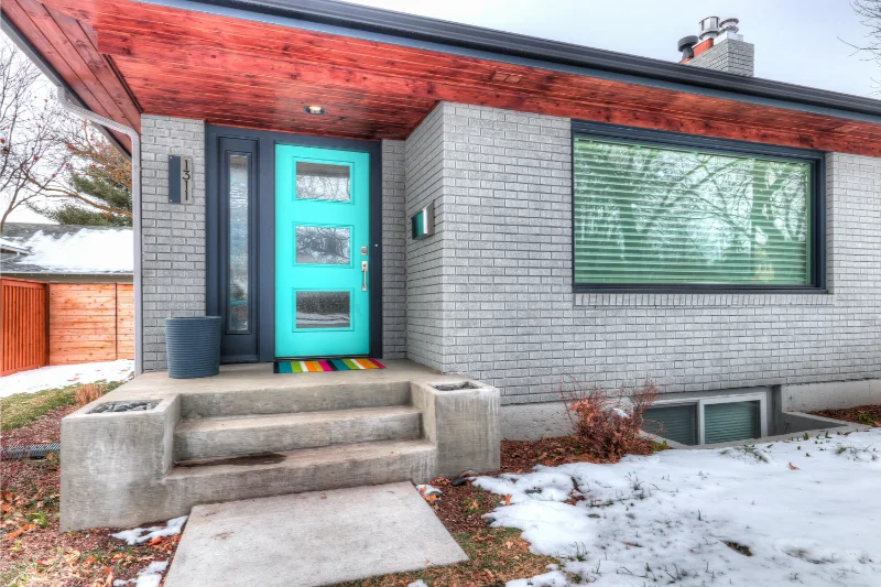 Teal front door on gray brick house, red overhang, snow on ground.
