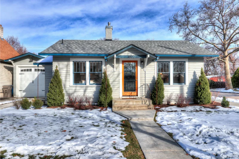 Cozy white house with snow-covered yard, a gray roof, and a welcoming front door.