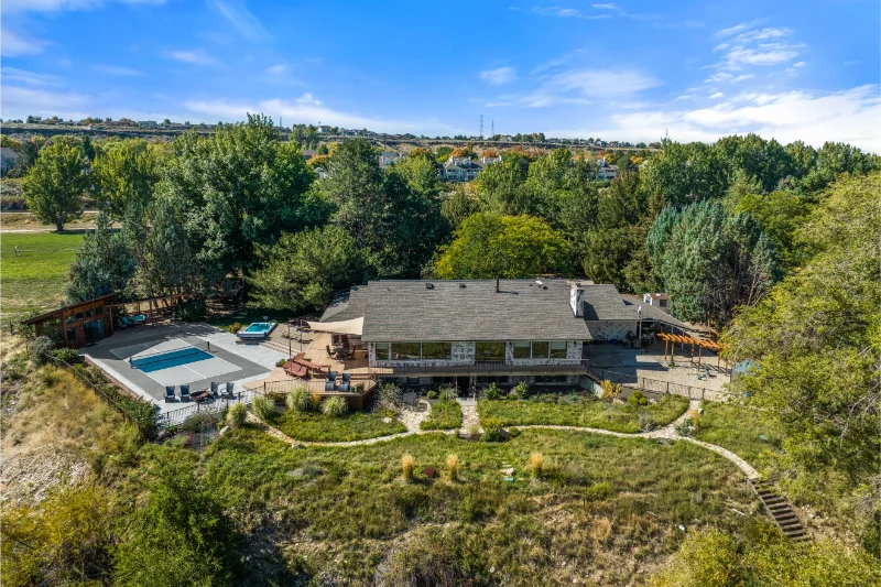 Aerial view of a home with a pool, deck, and surrounding trees on a hillside.